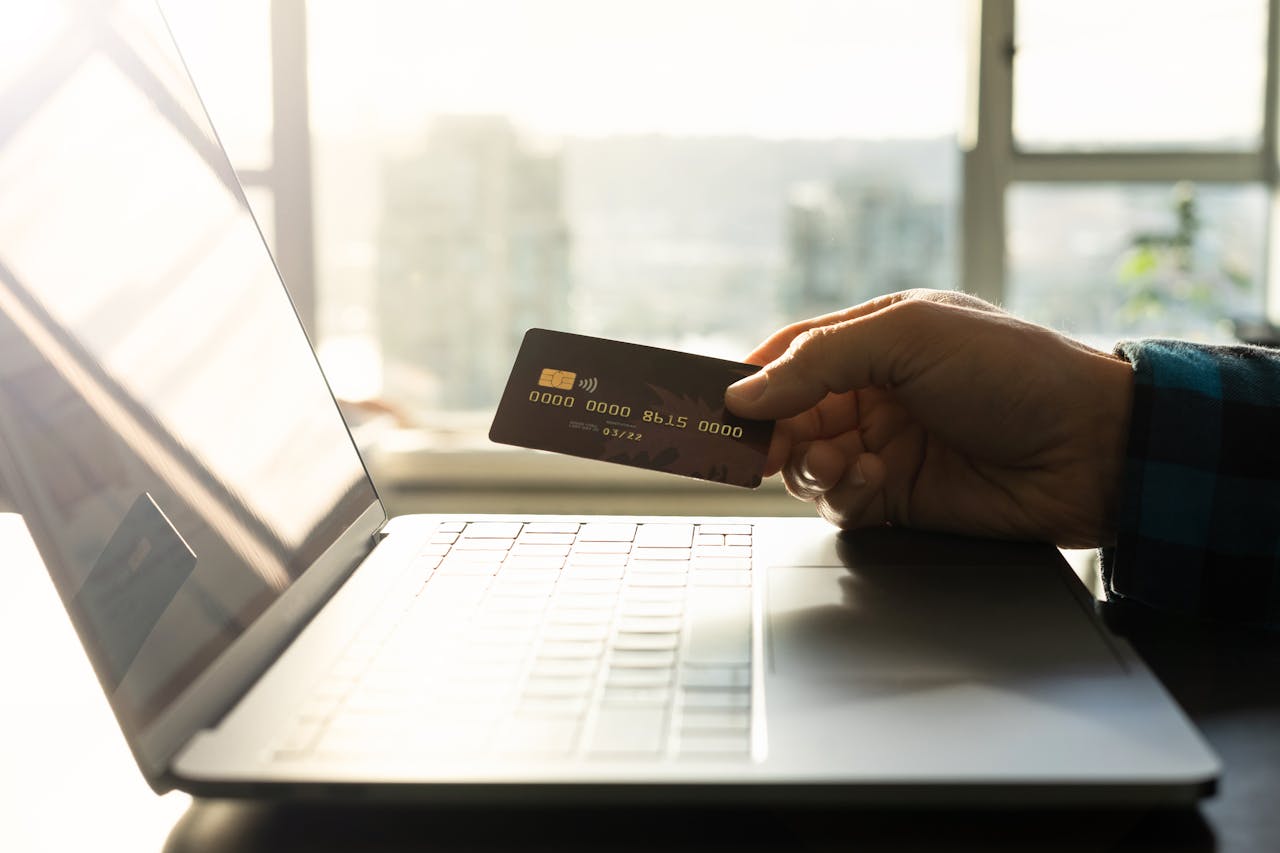 A hand holding a credit card in front of a laptop, symbolizing online shopping and digital payment.